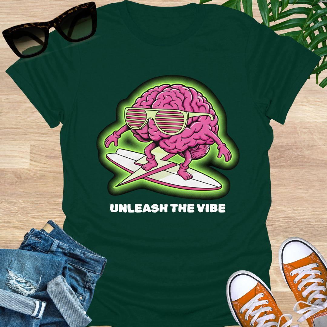 Pink cartoon brain wearing sunglasses surfing on a board with green glow and the words “Unleash the Vibe” on a forrest green t-shirt