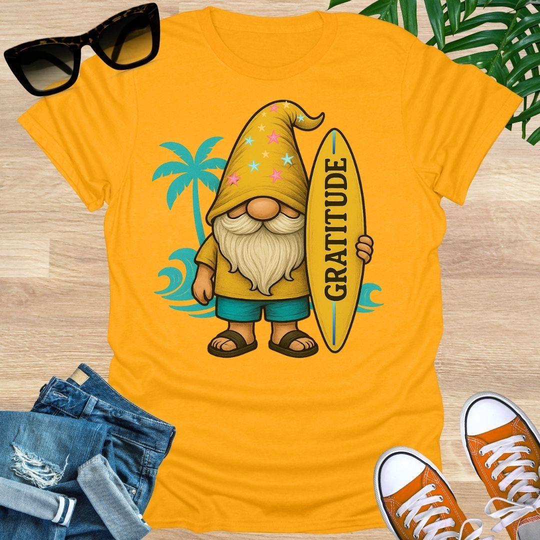Yellow t-shirt with a gnome holding a 'Gratitude' surfboard on a wooden surface with sunglasses, jeans, and shoes.