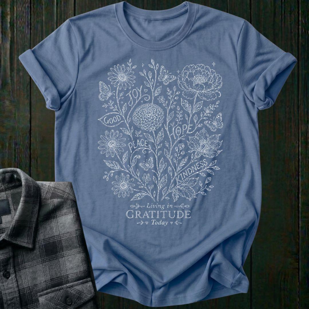 Vintage botanical illustration featuring flowers, butterflies, leaves, and the inspirational words joy, hope, peace, kindness, and good above the phrase Living in Gratitude Today on a indigo blue shirt