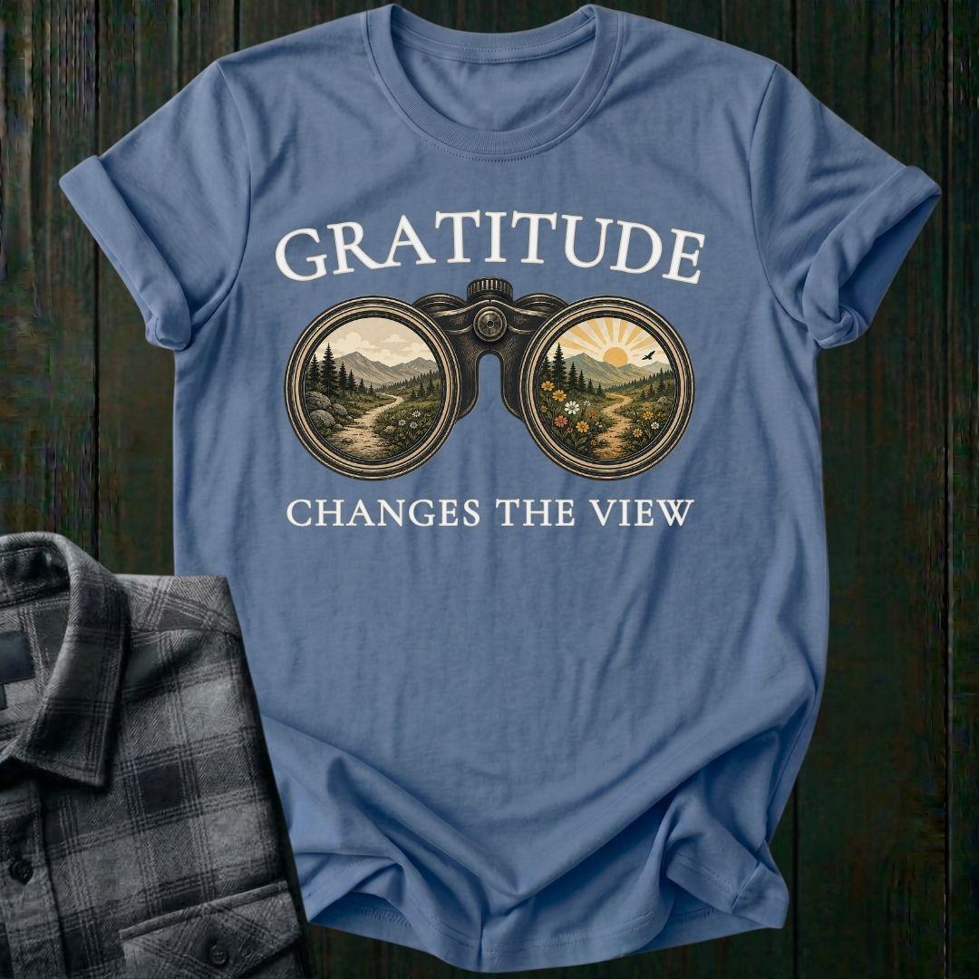 Vintage binoculars graphic showing two landscapes, one ordinary and one bright and colorful, with the phrase "Gratitude Changes the View" on a indigo blue tee