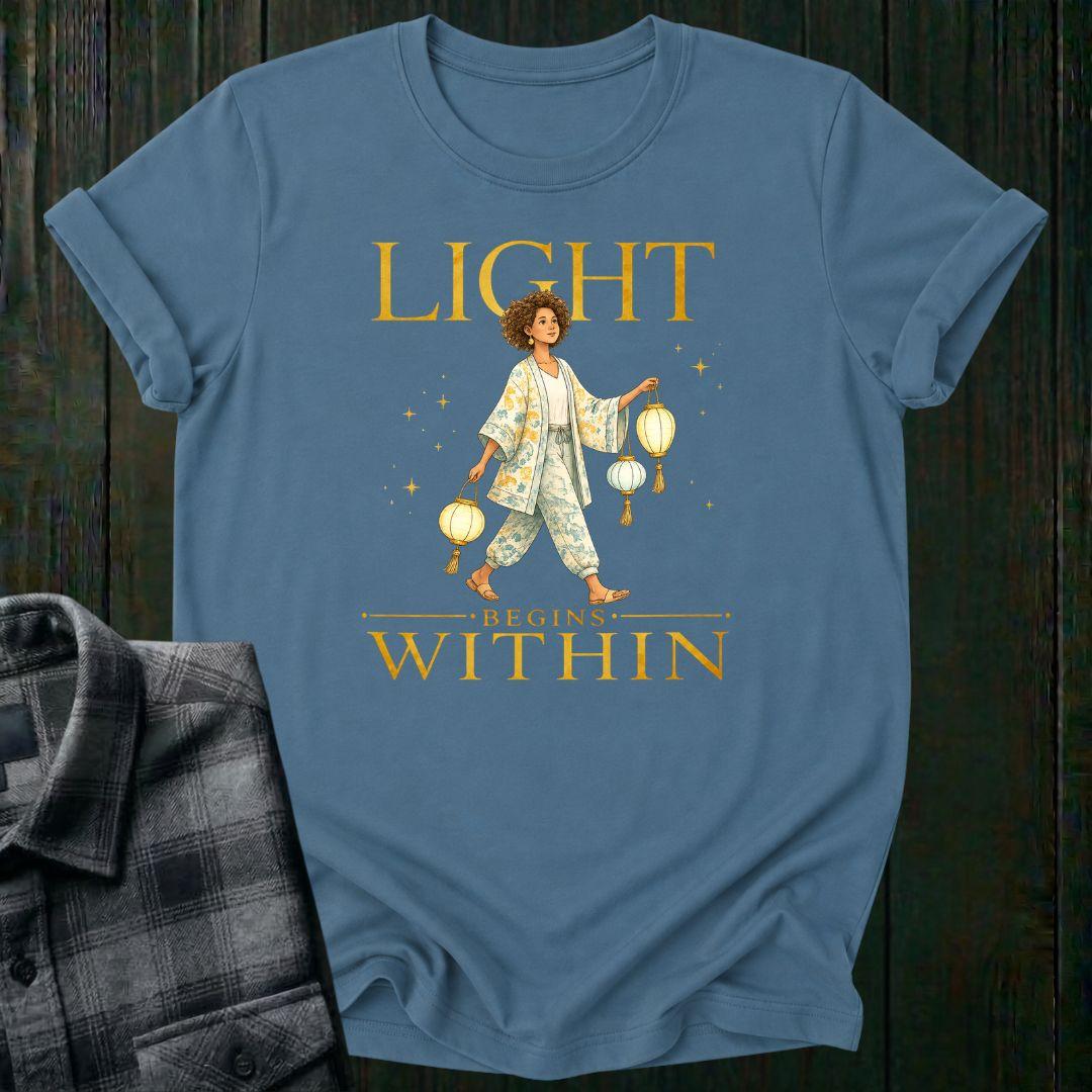 Illustrated woman carrying glowing paper lanterns beneath the words "Light Begins Within," symbolizing inner light, hope, mindfulness, and personal growth on a light blue tee