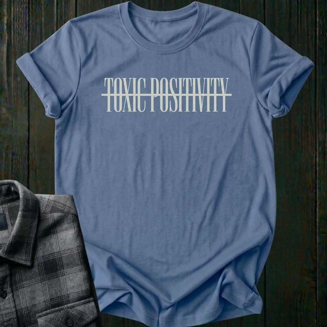 Indigo blue tee with minimalist typography design featuring the phrase "No More Toxic Positivity" in bold modern lettering with a horizontal line running through the center of the text.