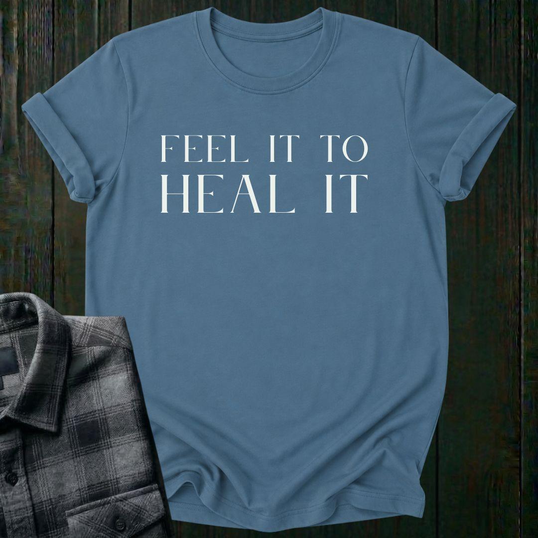 Minimalist typography design featuring the phrase "Feel It to Heal It" in elegant serif lettering on an indigo blue tee.