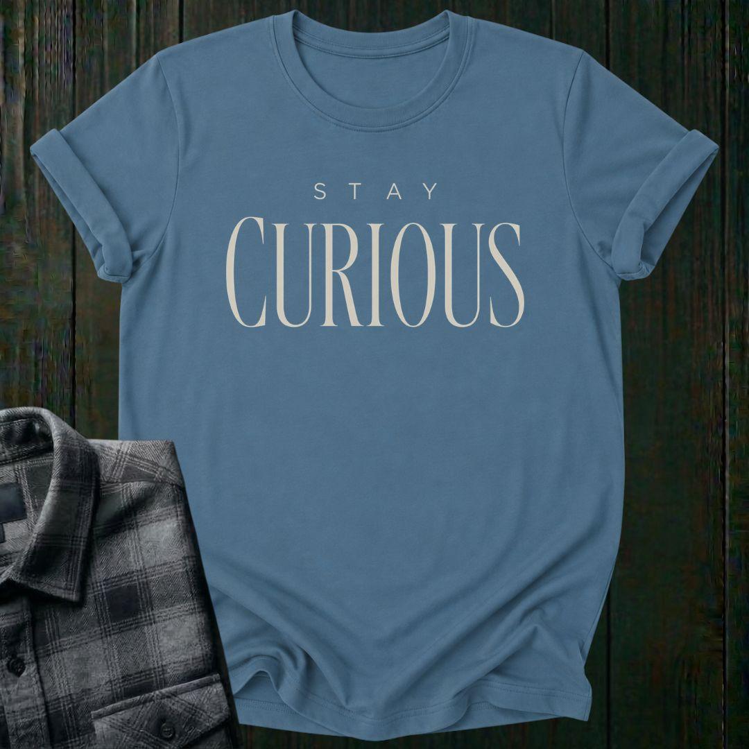 Elegant minimalist typography design featuring the phrase "Stay Curious" in refined serif lettering on an indigo blue tee.