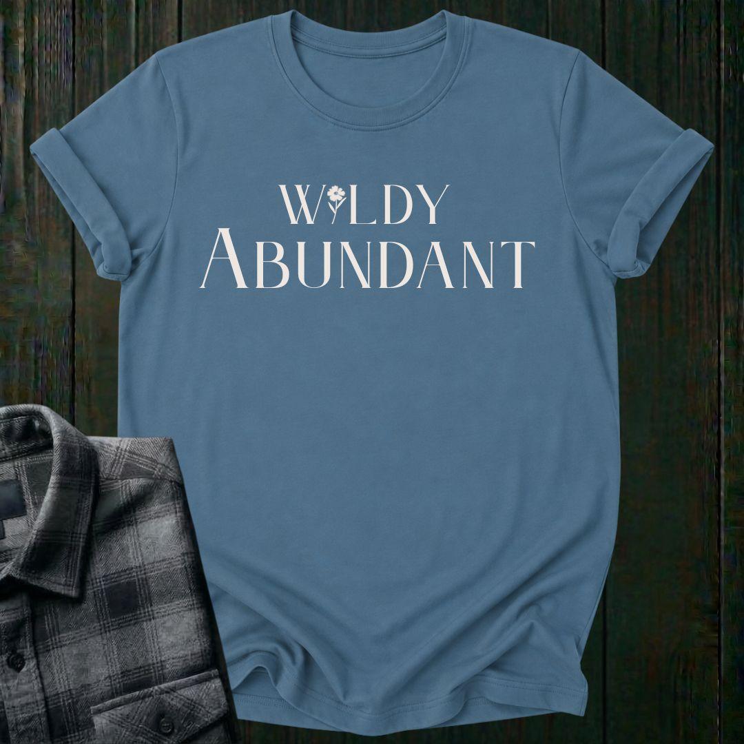 Elegant typography design featuring the phrase "Wildly Abundant" with a flower replacing the letter I in Wildly on an indigo blue tee.