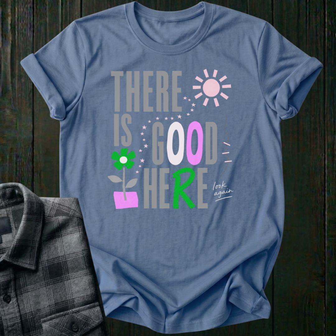 Colorful typography design featuring the phrase "There Is Good Here" with flowers, stars, sunshine, and the handwritten words "look again" on a indigo blue tee.