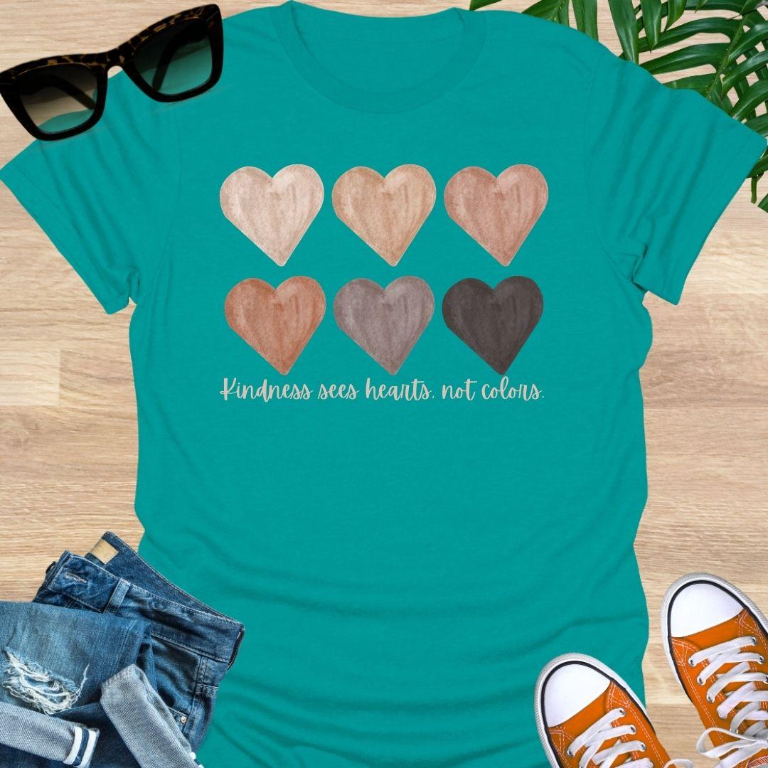 Teal t-shirt with six watercolor hearts in diverse skin tones above the script “Kindness sees hearts, not colors” on a unisex tee.