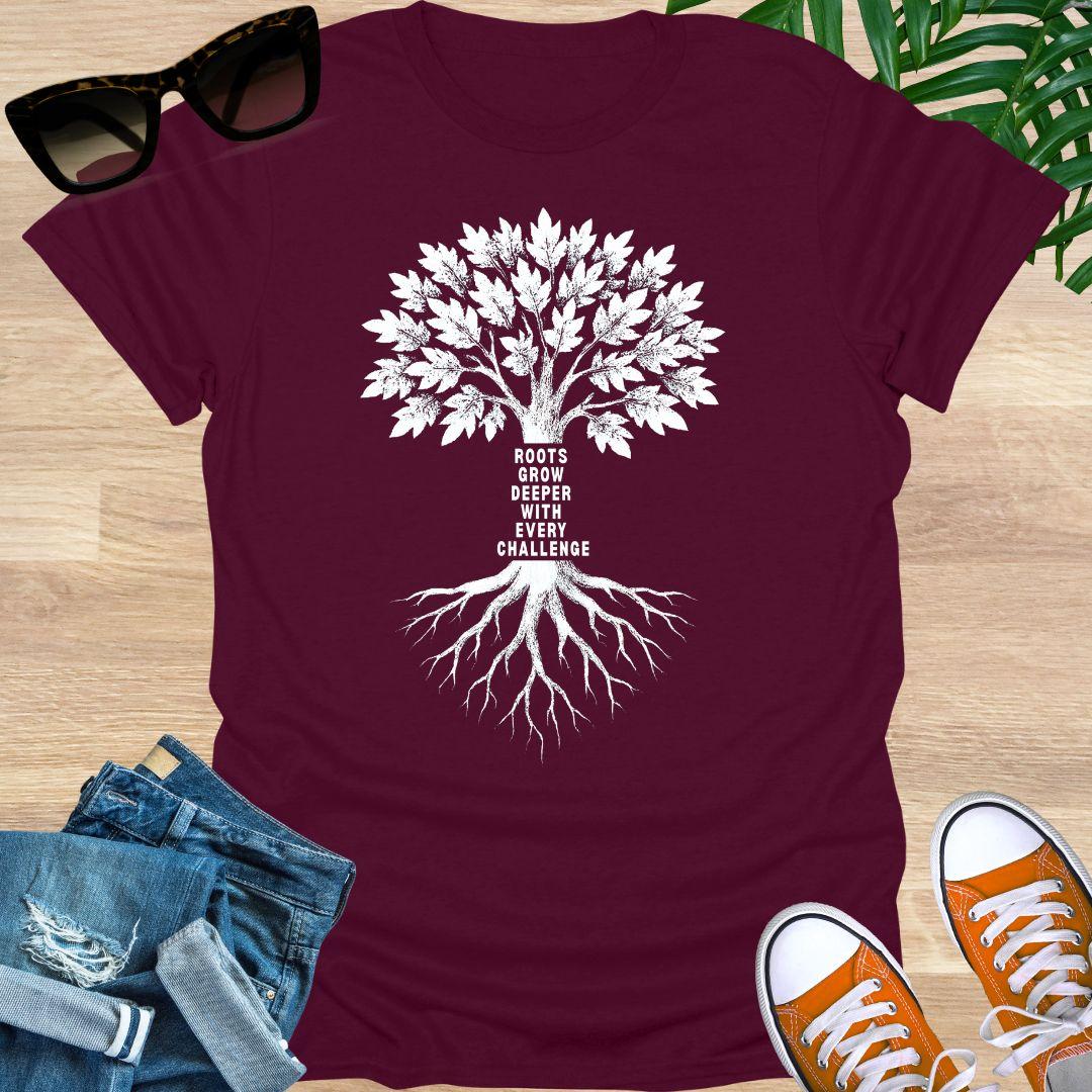 White tree with deep roots and the phrase “Roots grow deeper with every challenge” on a maroon unisex tee.