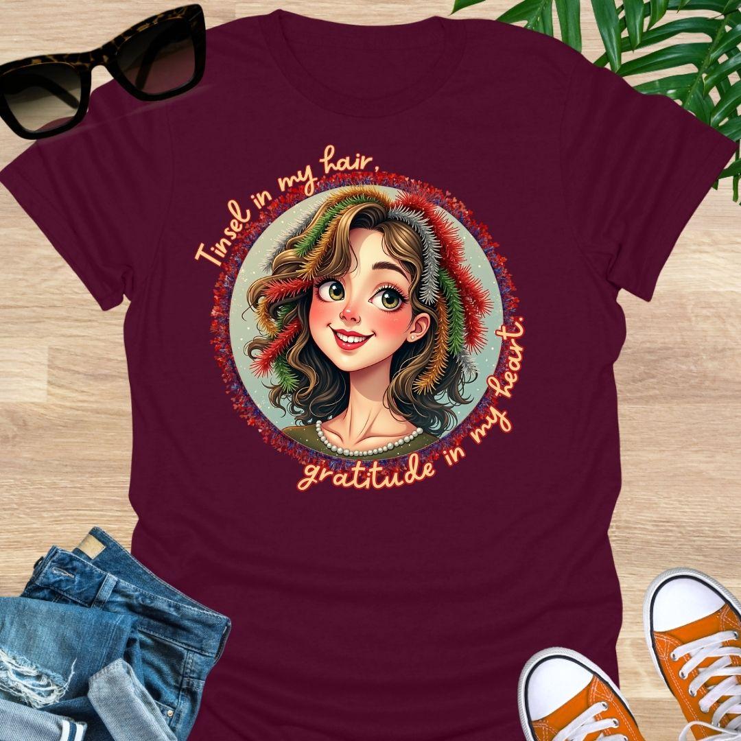 Smiling holiday portrait with colorful tinsel and the phrase “Tinsel in my hair, gratitude in my heart” on a maroon unisex festive tee.