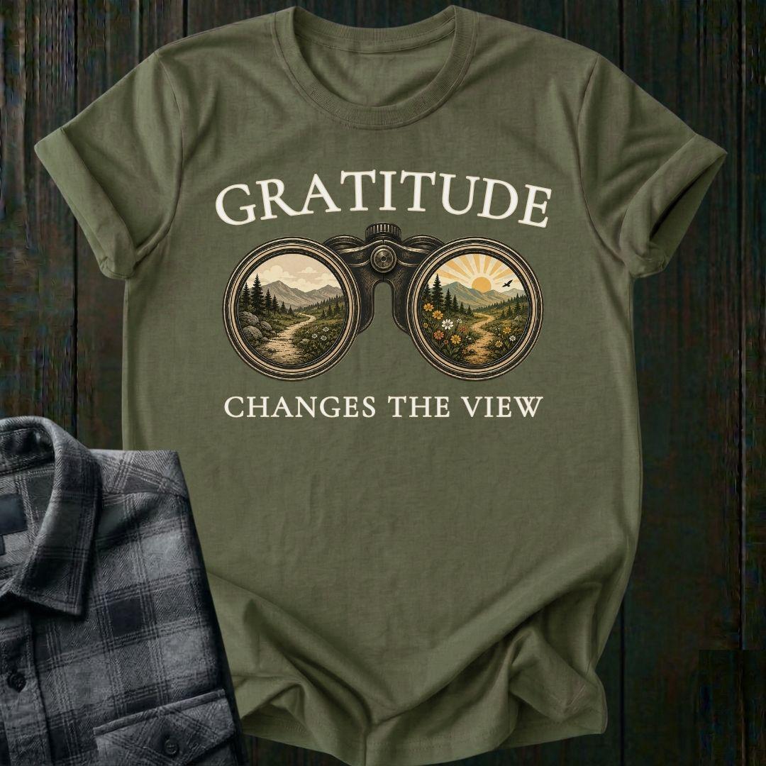 Vintage binoculars graphic showing two landscapes, one ordinary and one bright and colorful, with the phrase "Gratitude Changes the View" on a military green tee