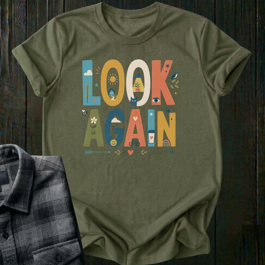 Colorful typography design featuring the phrase "Look Again" filled with cheerful illustrations including a house, sunshine, flowers, coffee cup, bicycle, rainbow, cat, and bird on a military green tee