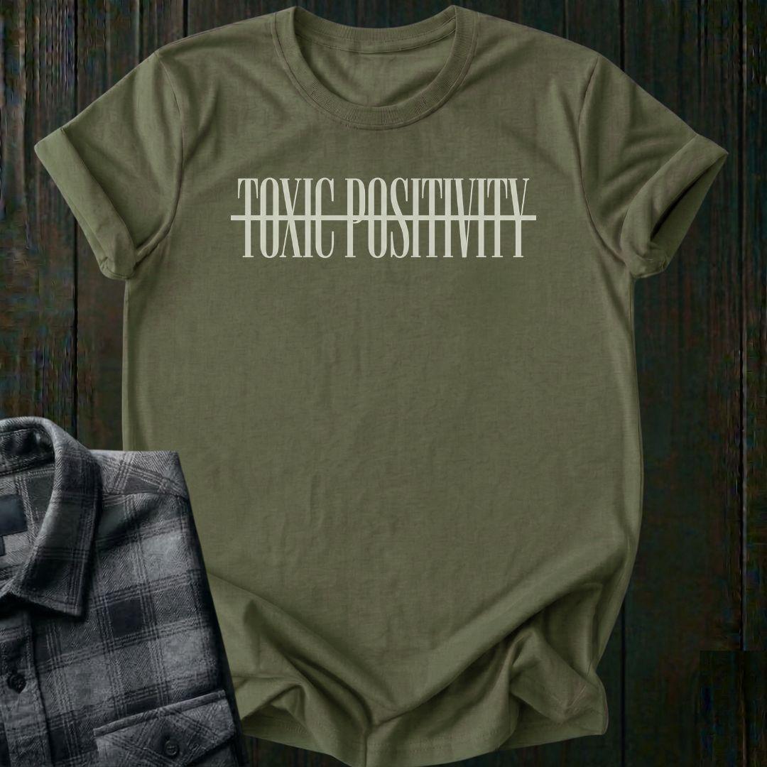 Military Green tee with minimalist typography design featuring the phrase "No More Toxic Positivity" in bold modern lettering with a horizontal line running through the center of the text.