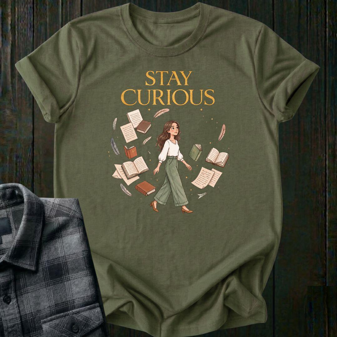 Illustrated woman walking among floating books, journals, feathers, and stars beneath the words "Stay Curious," symbolizing lifelong learning, creativity, and wonder on a military green tee.