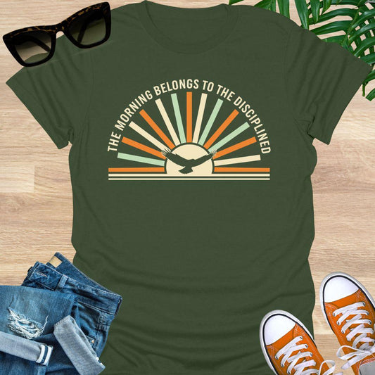 Sunrise with eagle silhouette and Morning Belongs to the Disciplined message symbolizing discipline, focus, growth, and success mindset on a military green tee