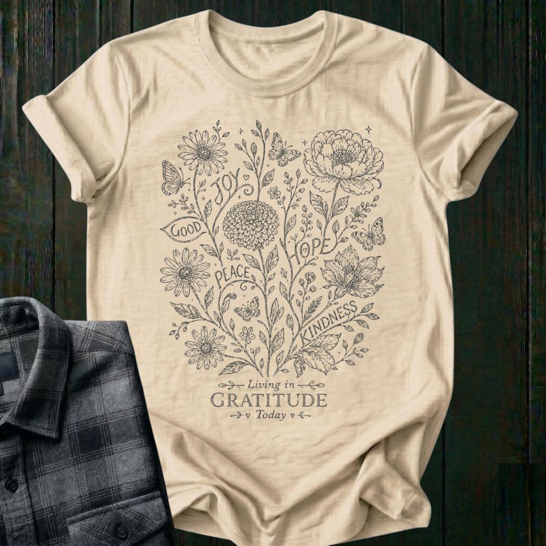 Vintage botanical illustration featuring flowers, butterflies, leaves, and the inspirational words joy, hope, peace, kindness, and good above the phrase Living in Gratitude Today on a beige shirt