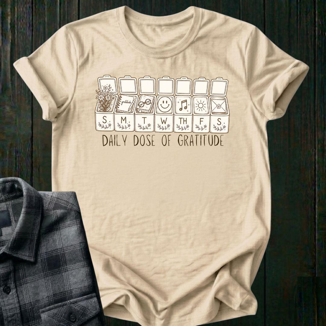 Vintage-inspired weekly pill organizer graphic featuring gratitude-themed icons for each day of the week, including flowers, journaling, reading, smiling, music, sunshine, and connection, with the phrase Daily Dose of Gratitude on a natural tee