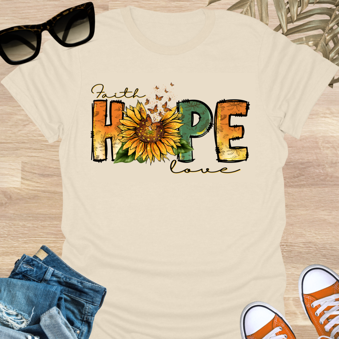 Beige t-shirt with a sunflower and monarch butterflies between the words "Faith, Hope, Love" on a unisex graphic tee.