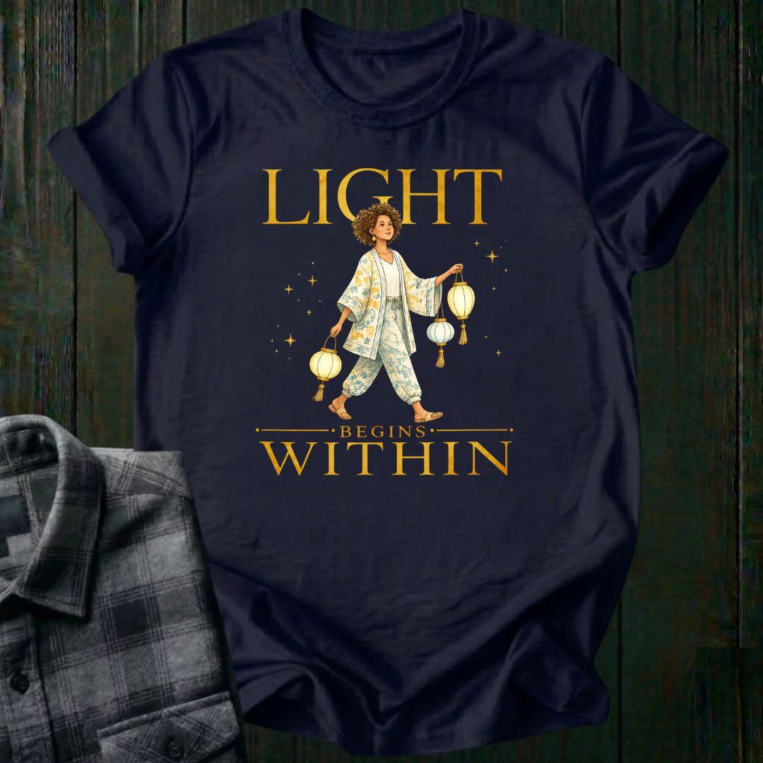 Illustrated woman carrying glowing paper lanterns beneath the words "Light Begins Within," symbolizing inner light, hope, mindfulness, and personal growth on a navy tee