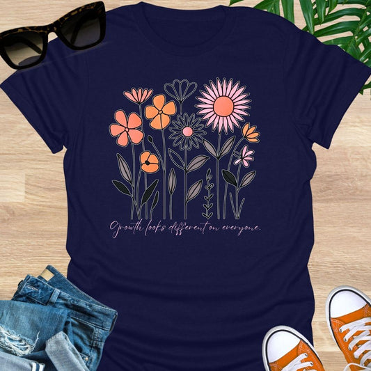 Navy blue unisex t-shirt. Hand-drawn wildflowers with the script “Growth looks different on everyone” 