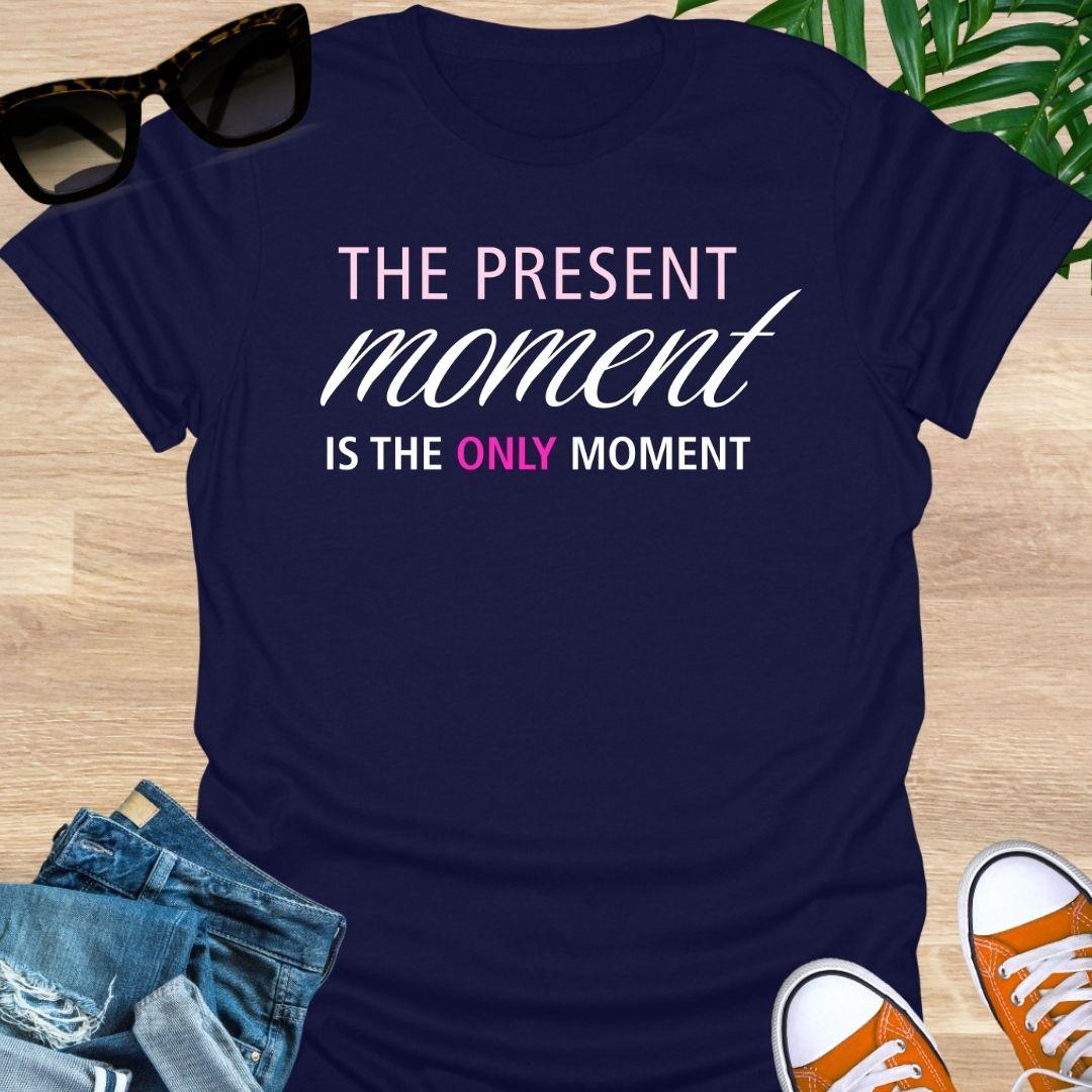 Navy tee with pink/white text reading “The Present Moment Is the Only Moment” minimalist mindfulness graphic.