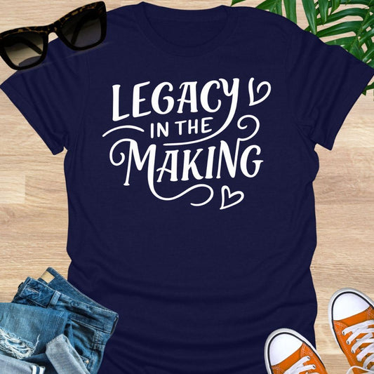 White script “Legacy in the Making” with heart flourishes on a navy motivational graphic tee.