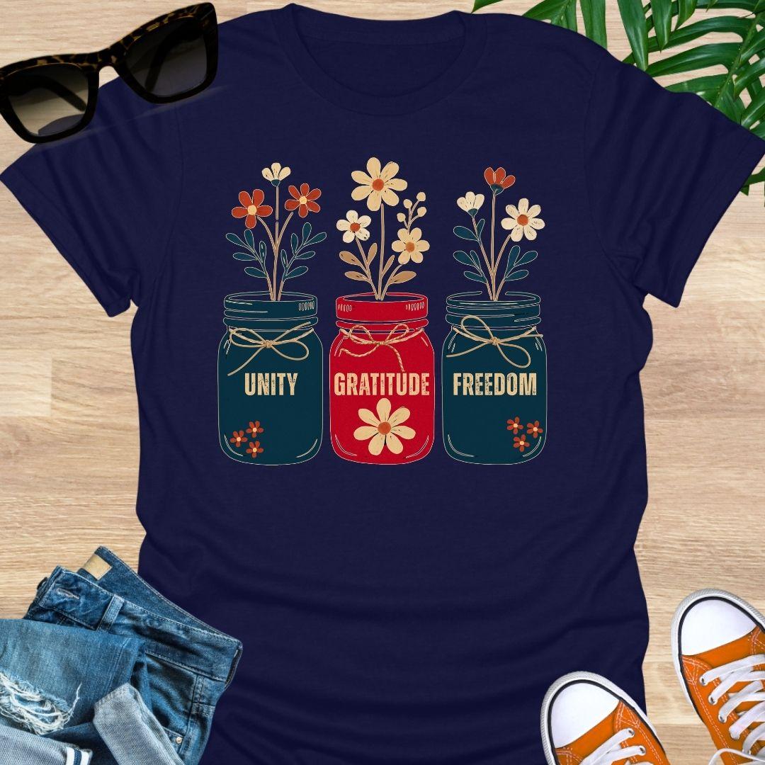 Three mason jars labeled Unity, Gratitude, Freedom with wildflowers in Americana colors on a navy unisex graphic tee.