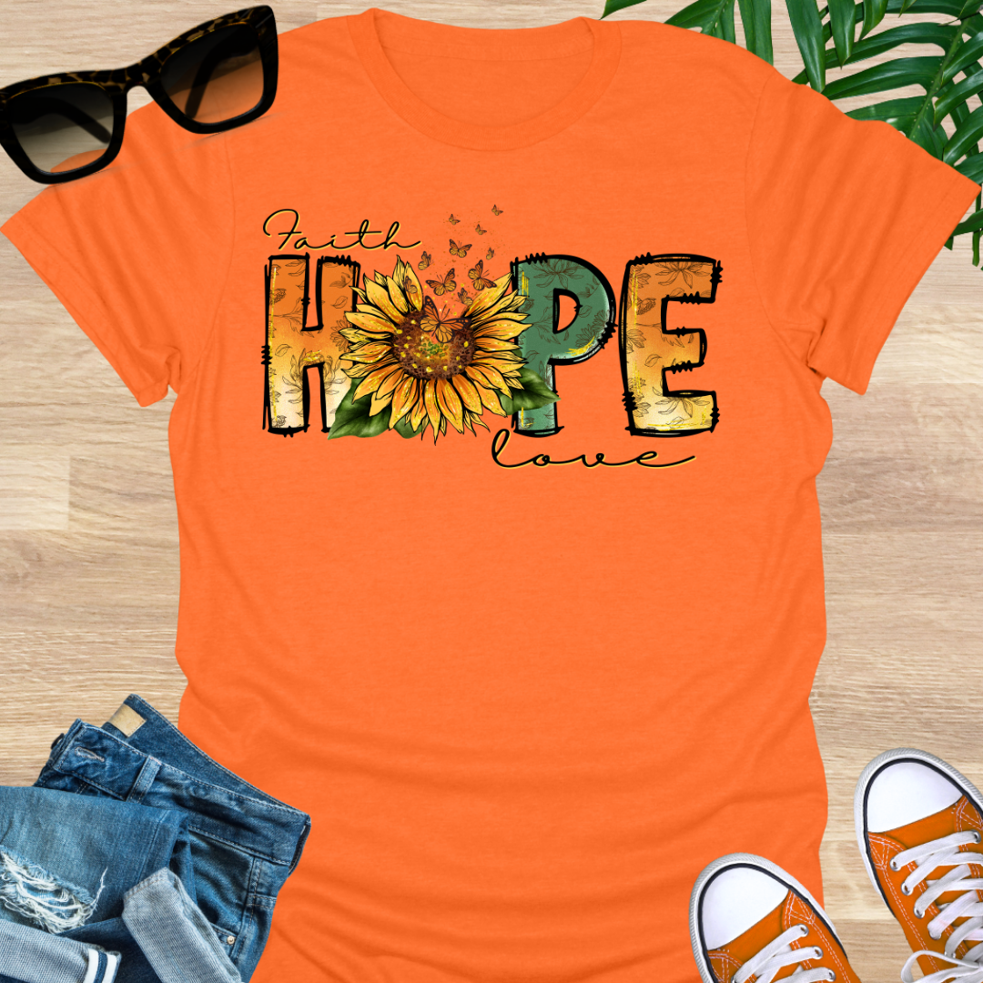 Orange t-shirt with a sunflower and monarch butterflies between the words "Faith, Hope, Love" on a unisex graphic tee.