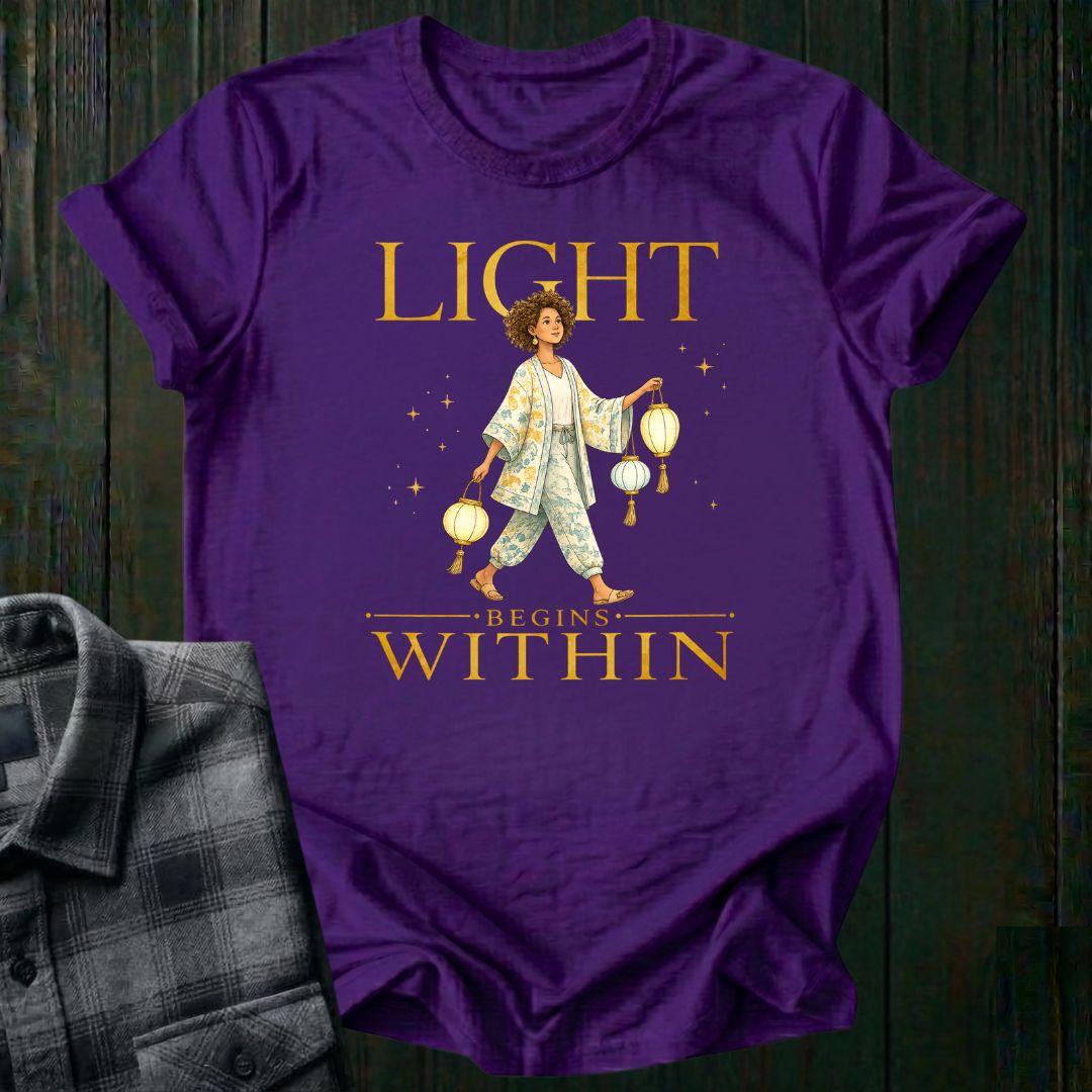 Illustrated woman carrying glowing paper lanterns beneath the words "Light Begins Within," symbolizing inner light, hope, mindfulness, and personal growth on a purple tee