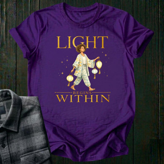 Illustrated woman carrying glowing paper lanterns beneath the words "Light Begins Within," symbolizing inner light, hope, mindfulness, and personal growth on a purple tee