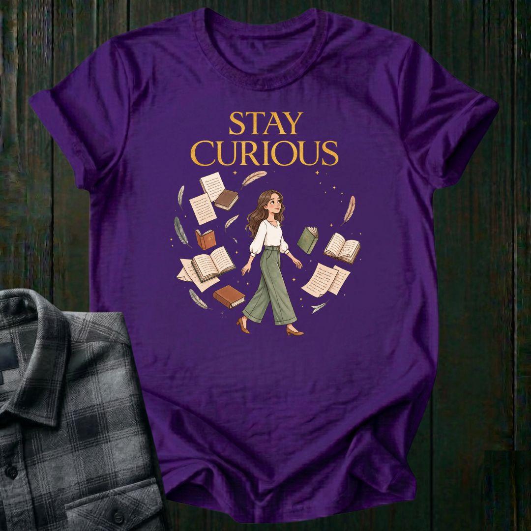 Illustrated woman walking among floating books, journals, feathers, and stars beneath the words "Stay Curious," symbolizing lifelong learning, creativity, and wonder on a purple tee.