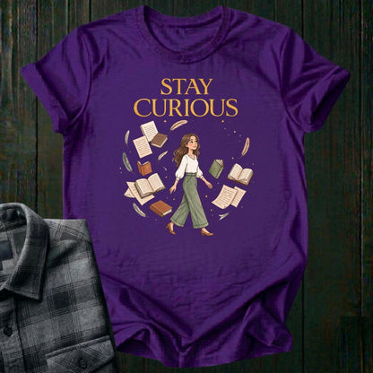 Illustrated woman walking among floating books, journals, feathers, and stars beneath the words "Stay Curious," symbolizing lifelong learning, creativity, and wonder on a purple tee.