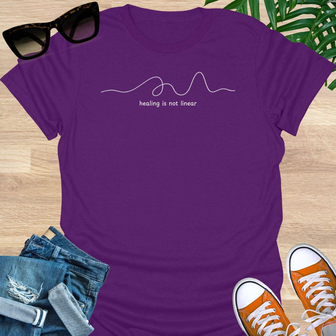 Purple unisex t-shirt with minimalist line art and white text reading healing is not linear