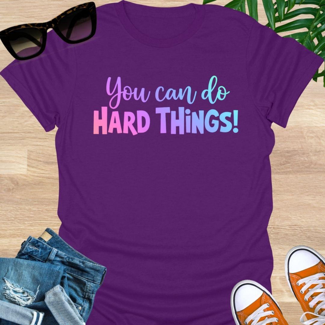 “You Can Do Hard Things” in sunrise gradient lettering on a purple unisex tee.