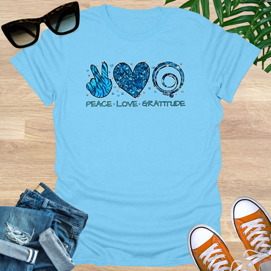 Light blue unisex T-shirt with peace sign, heart, and spiral text reading “Peace • Love • Gratitude.”