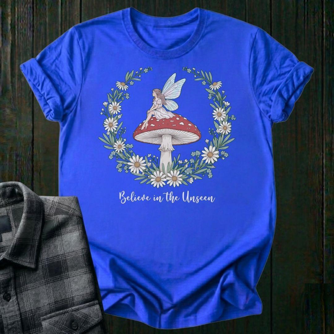 Blue t-shirt with fairy and mushroom design on a wooden surface