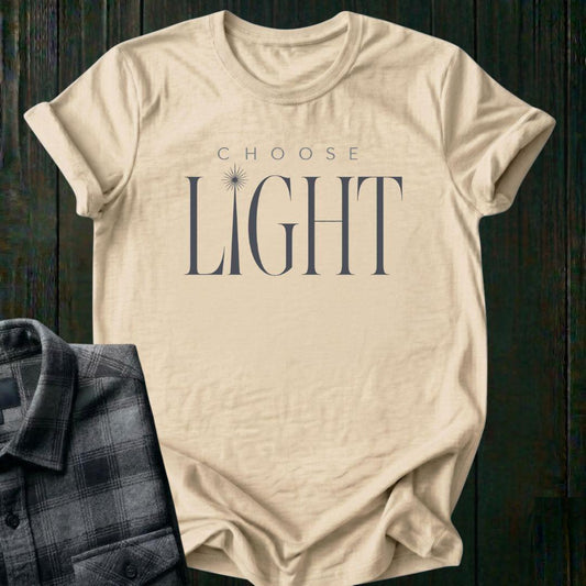 Elegant minimalist typography design featuring the phrase "Choose Light" with a radiant sunbeam replacing the letter I in "Light" on a beige tee