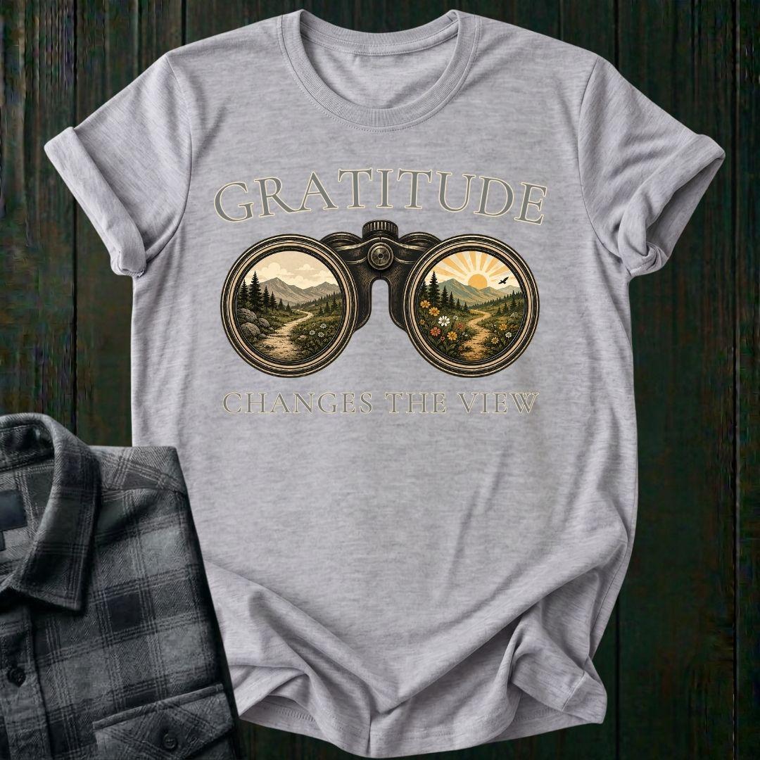 Vintage binoculars graphic showing two landscapes, one ordinary and one bright and colorful, with the phrase "Gratitude Changes the View" on a light gray tee