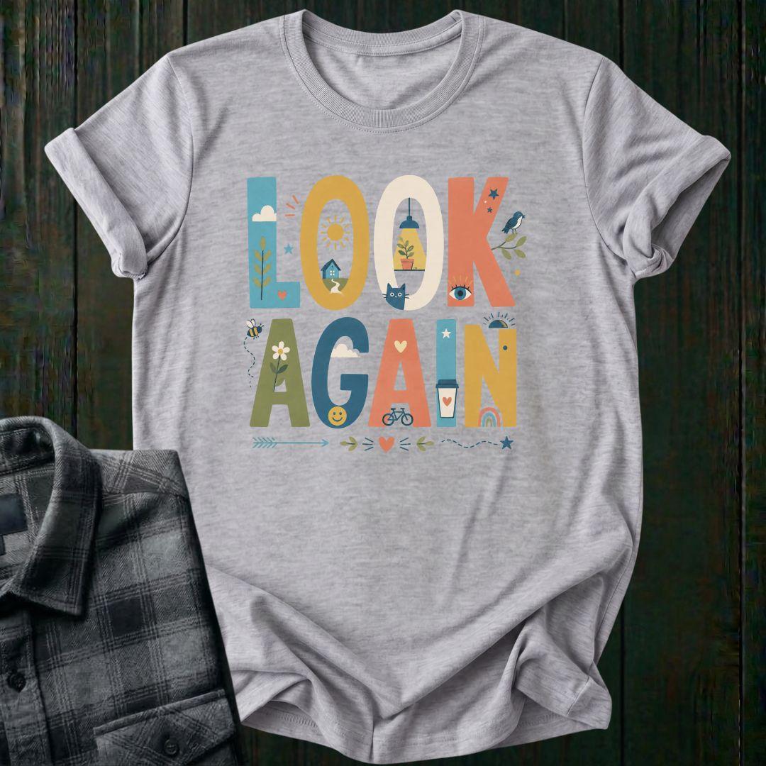 Colorful typography design featuring the phrase "Look Again" filled with cheerful illustrations including a house, sunshine, flowers, coffee cup, bicycle, rainbow, cat, and bird on a light gray tee